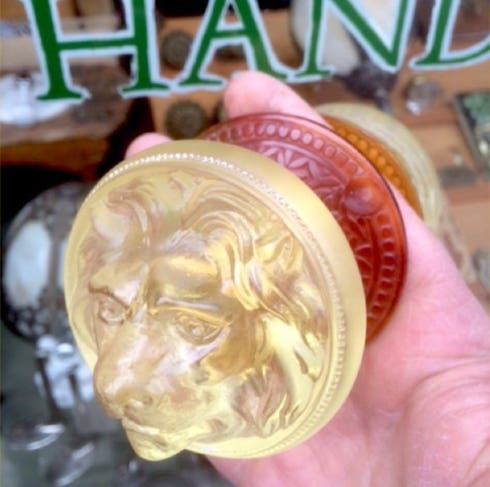 Hand holding a translucent amber lion's head doorknob beside a red patterned knob