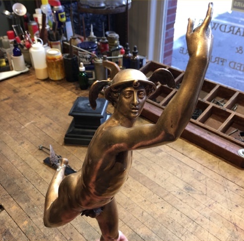 Bronze Mercury statue with winged helmet and raised arm standing in the workshop