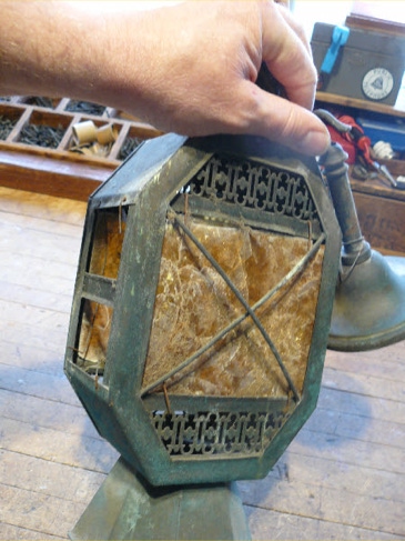 Hand holding an antique octagonal bronze porch lantern with torn mica panels