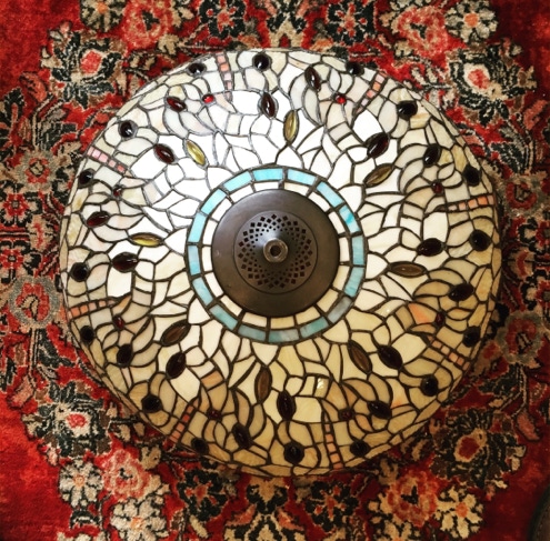 Large Tiffany style leaded glass dome shade laid face up on a red patterned rug