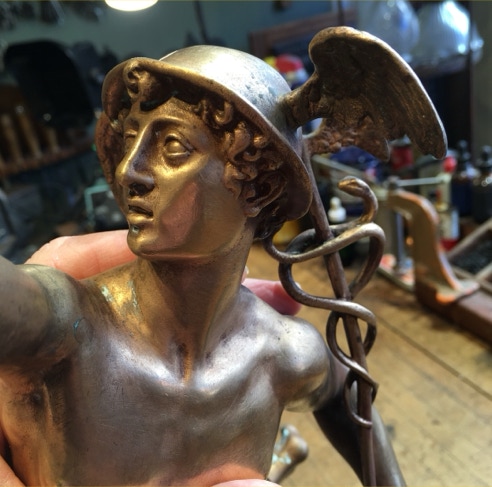Hand holding a cast bronze figure of Mercury with winged helmet and caduceus in the workshop