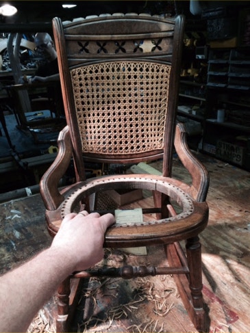 Antique cane-back rocking chair on a workbench with the seat frame removed for re-caning