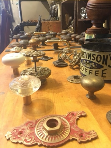 Rows of vintage glass, porcelain and brass doorknobs with decorative backplates on a workbench