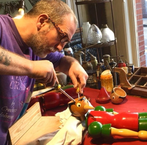 A restorer repairing the head of a vintage wooden Pinocchio toy