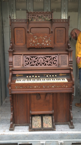 Ornate Eastlake style walnut pump organ with fretwork panels and foot pedals, freshly unloaded from a moving pod