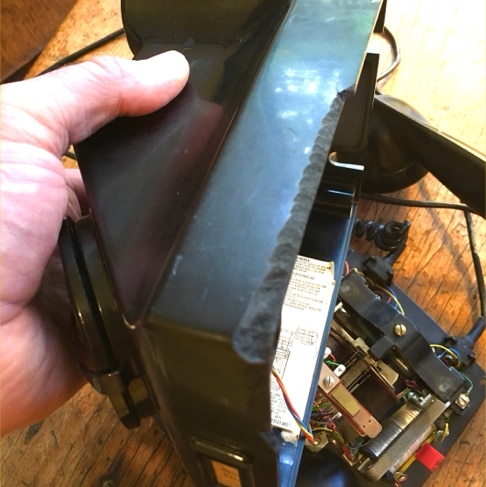 Hand holding the cracked bakelite telephone chassis with a missing chunk along the edge