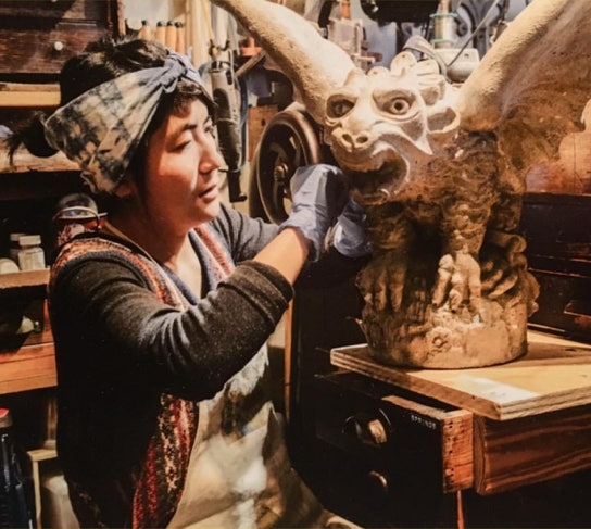 Koko applying final detail work to a large concrete griffin statue on a workbench