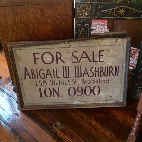 Hand-lettered antique For Sale real estate sign in a wooden frame leaning against a chest