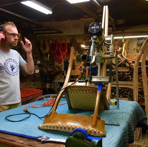 Restorer in hearing protection running a lock mortiser mounted to a chair part in the workshop