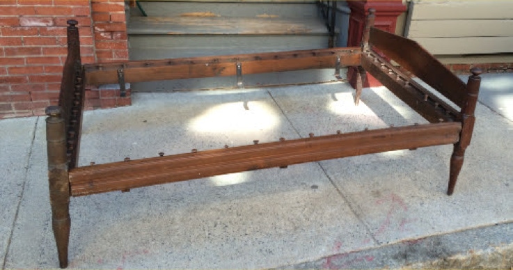 Antique 19th century Pennsylvania rope bed frame with turned posts standing outdoors on a sidewalk