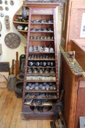 Tall wooden display shelf filled with antique doorknobs, hinges, light fixtures and salvaged hardware