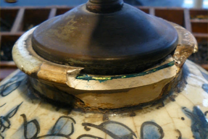 Close-up of a blue and white ceramic vase lamp with large chips missing around the rim