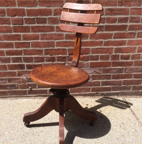Antique oak Cook Quality swivel office chair photographed against a brick wall