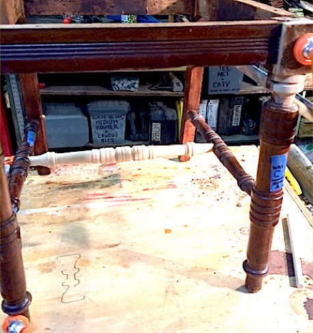 Underside of an antique side chair on a workbench showing a newly turned wood stretcher between the legs