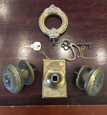 Antique brass doorknobs, a lock face, escutcheon and skeleton keys laid out on a dark wood surface