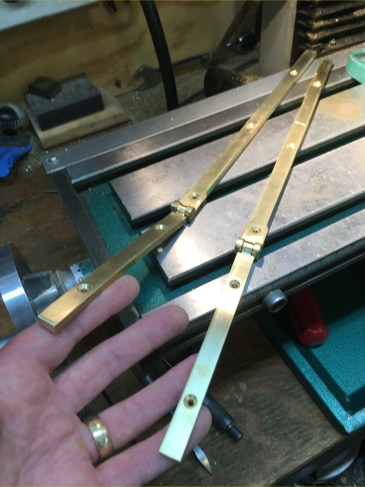 Hand holding two newly fabricated polished brass desk hinges above a milling machine table