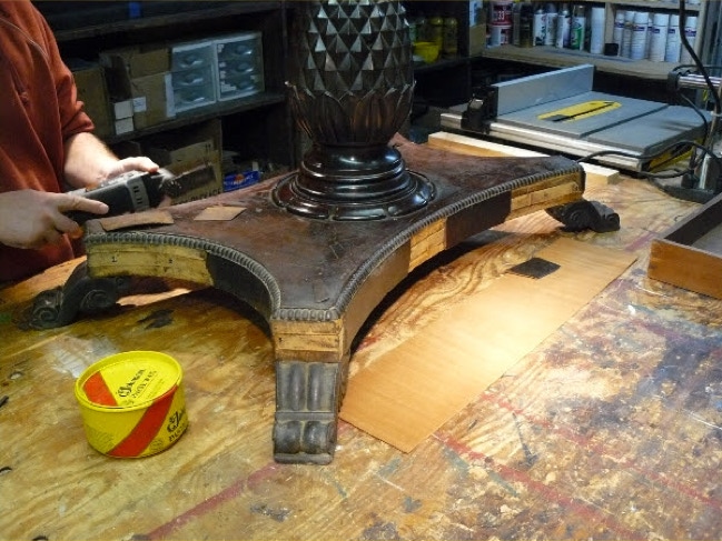 Craftsman removing damaged veneer from a carved antique table base on a workbench