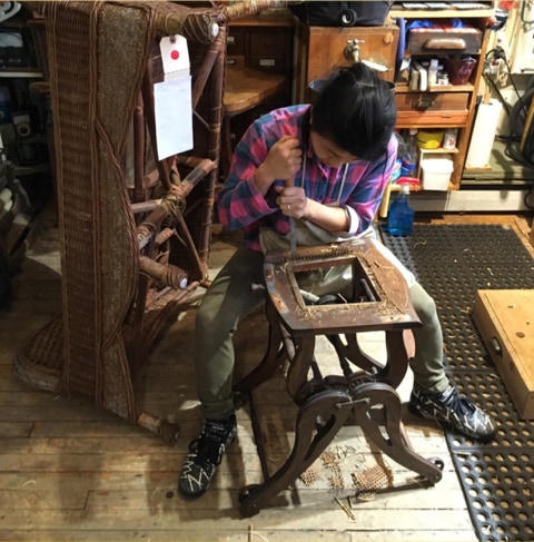 Koko chiseling old pressed cane and spline out of an antique high chair seat in the workshop