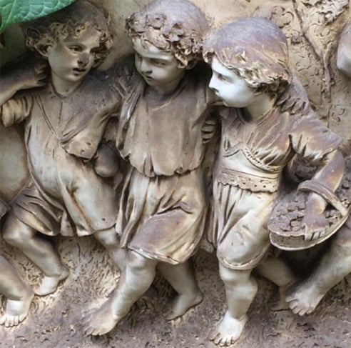 Detail of a plaster relief showing three children in robes carrying a basket of fruit
