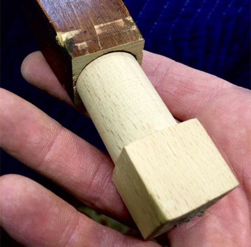 Hand holding an antique chair leg fitted with a freshly turned pale custom bumper