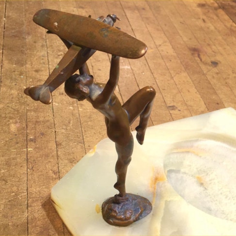 Bronze figure of a woman lifting a biplane overhead, standing upright on her onyx base