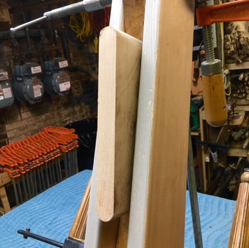 Freshly cut mortise slot in a wooden chair part clamped upright on the bench, ready for a hardwood spline