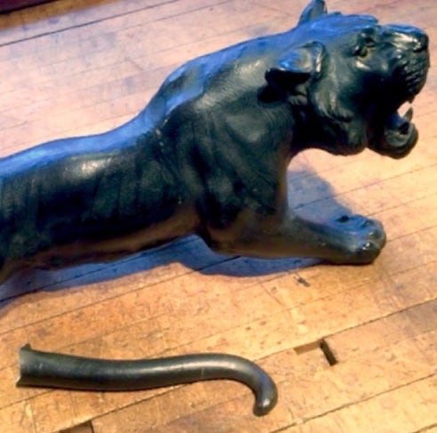 Cast metal cougar sculpture on a wood floor with its detached tail lying nearby