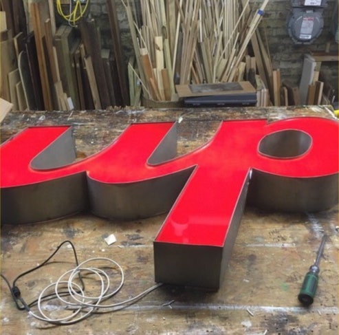 Large channel letters spelling up with new red acrylic faces sitting on a workshop bench