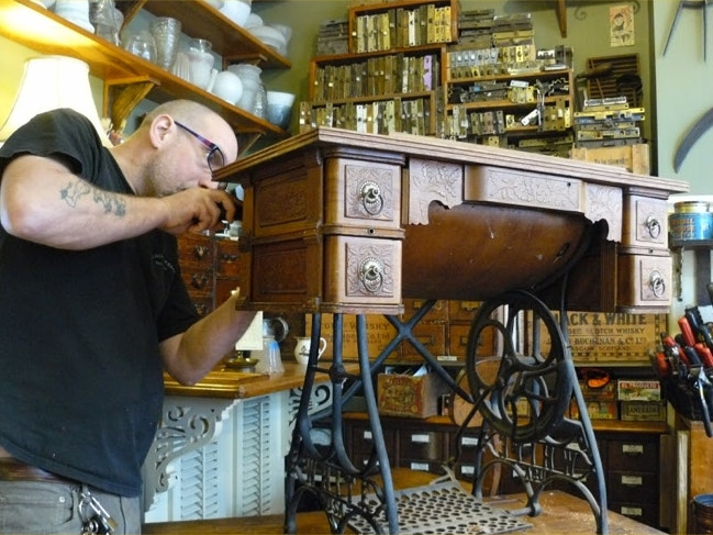 Restorer working on an ornate treadle sewing machine table with cast iron base in the workshop