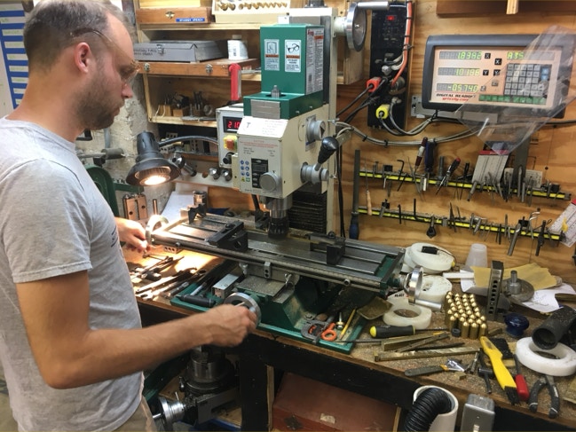 Craftsman machining brass hinge stock on a benchtop milling machine in a tool-lined machine shop