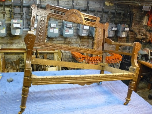 Stripped Eastlake loveseat frame with carved crest rail on a workbench awaiting upholstery