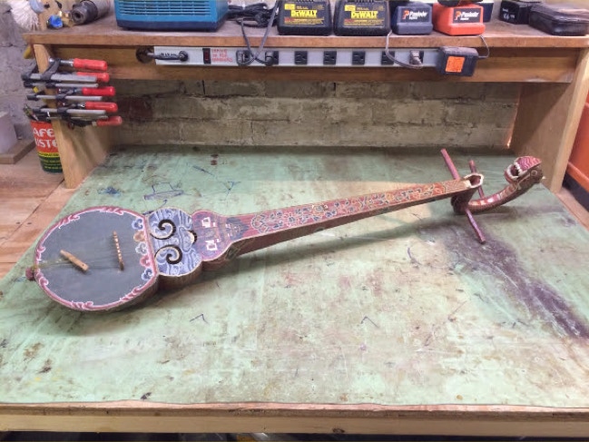Hand-painted dragon-faced oud stringed instrument laid out on a workshop bench