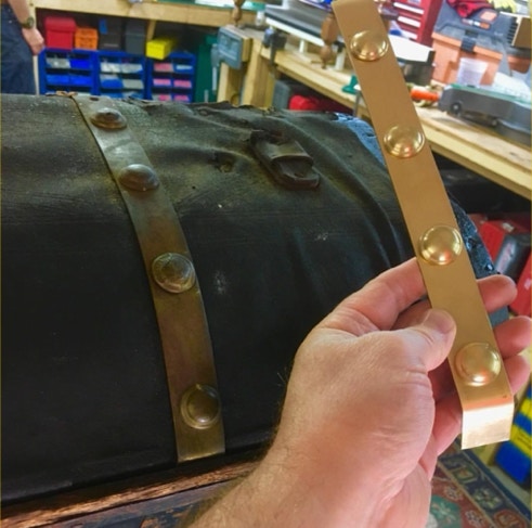 Restorer holding a newly fabricated brass trunk band with domed studs next to an antique trunk
