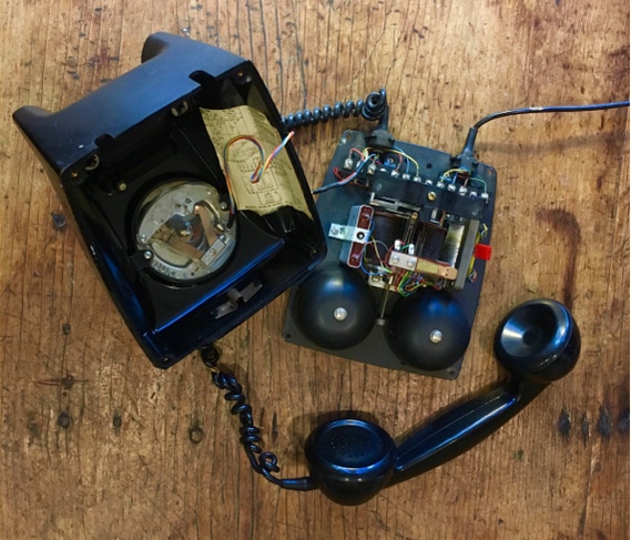 Opened bakelite Dutch Ericsson telephone showing dial mechanism, ringer bells and wiring on a workbench