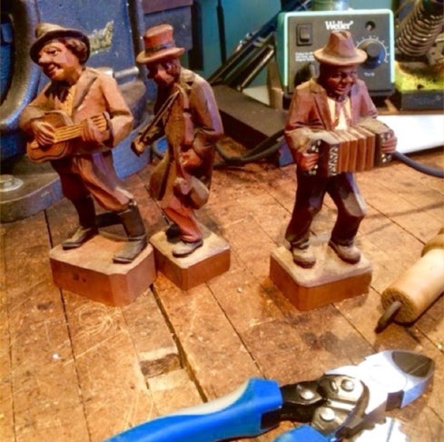 Three carved ANRI musician figurines on a workbench beside repair tools