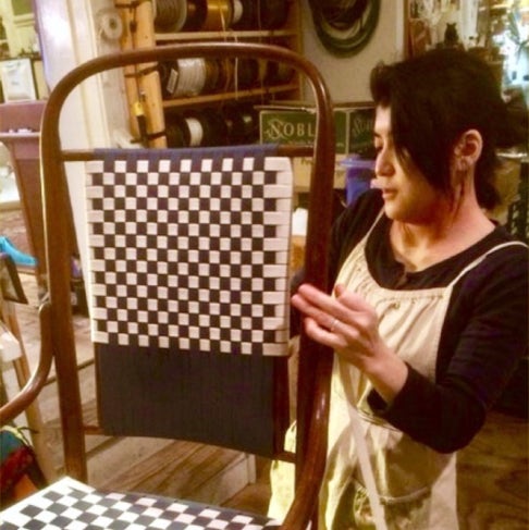 Koko weaving black and white Shaker tape into the seat and back of a bentwood rocking chair