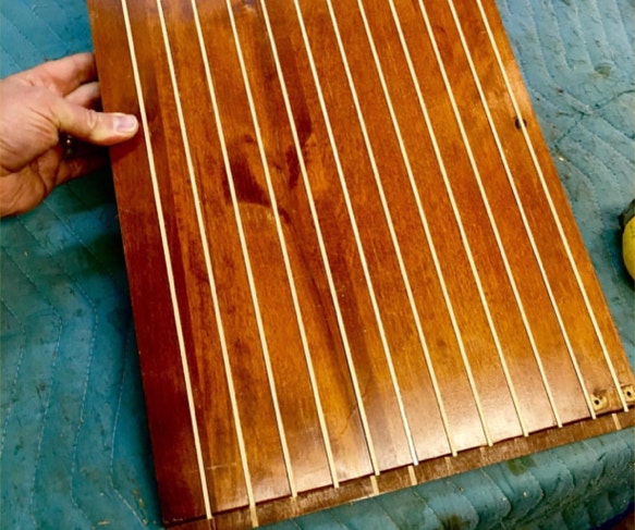 Hand holding a flattened cabinet door with pale maple splines running the length of its back face