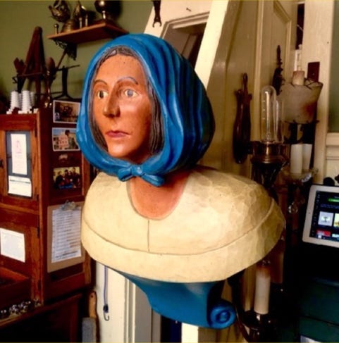 Carved and painted ship's figurehead of a woman in a blue headscarf mounted upright in the shop