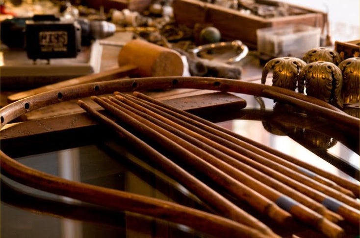Disassembled chair bow and spindles laid out on a workbench beside brass finials