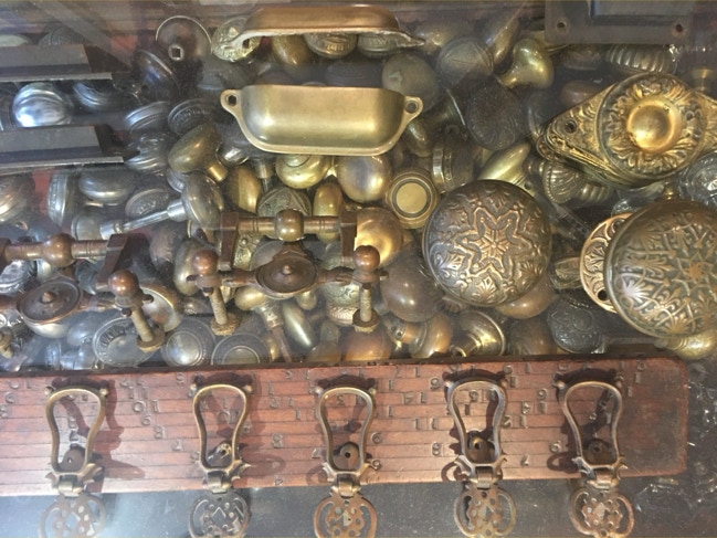 Display case packed with antique brass doorknobs, bin pulls and coat hooks