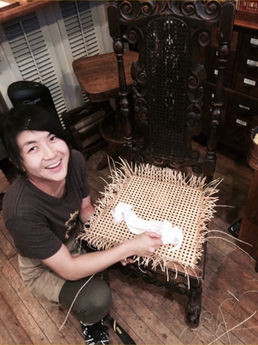 Restorer weaving a new hand-caned seat into a carved Spanish Revival chair in the workshop