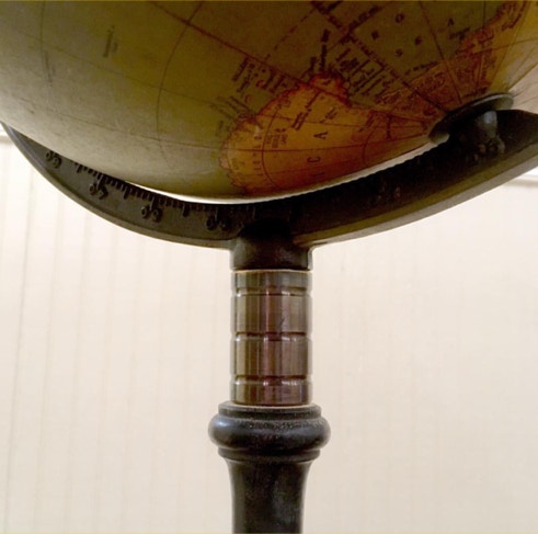 Antique terrestrial globe mounted on a dark turned candle stand with a machined brass collet