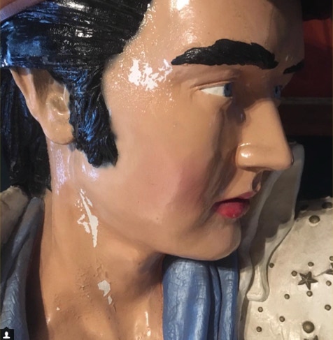 Close-up of a painted Elvis statue face mid-restoration with fresh white paint drips on the cheek and neck